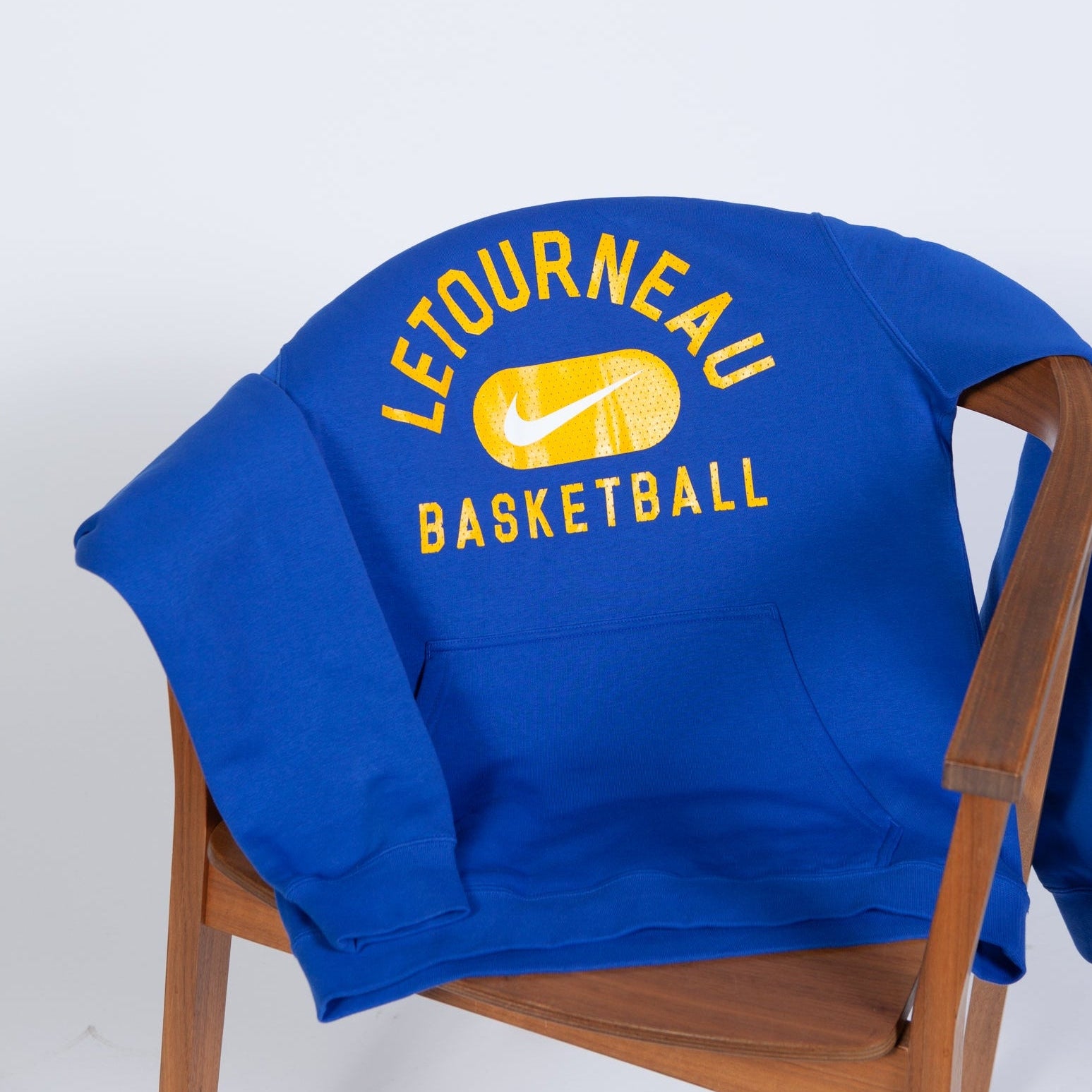 Blue sweatshirt with 'Letourneau Basketball' text on a wooden chair against a white background
