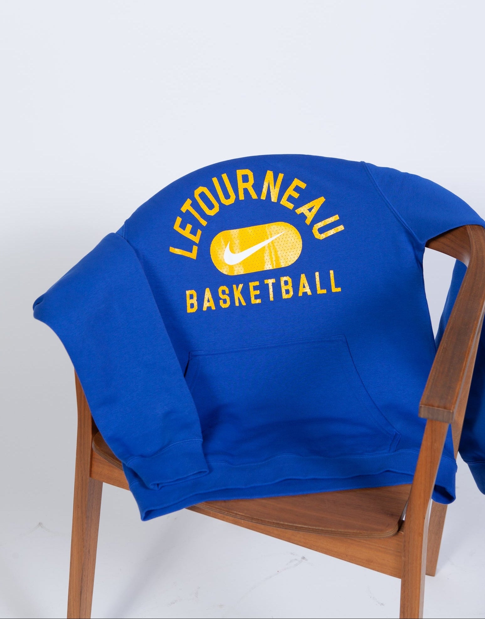 Blue sweatshirt with 'Letourneau Basketball' text on a wooden chair against a white background
