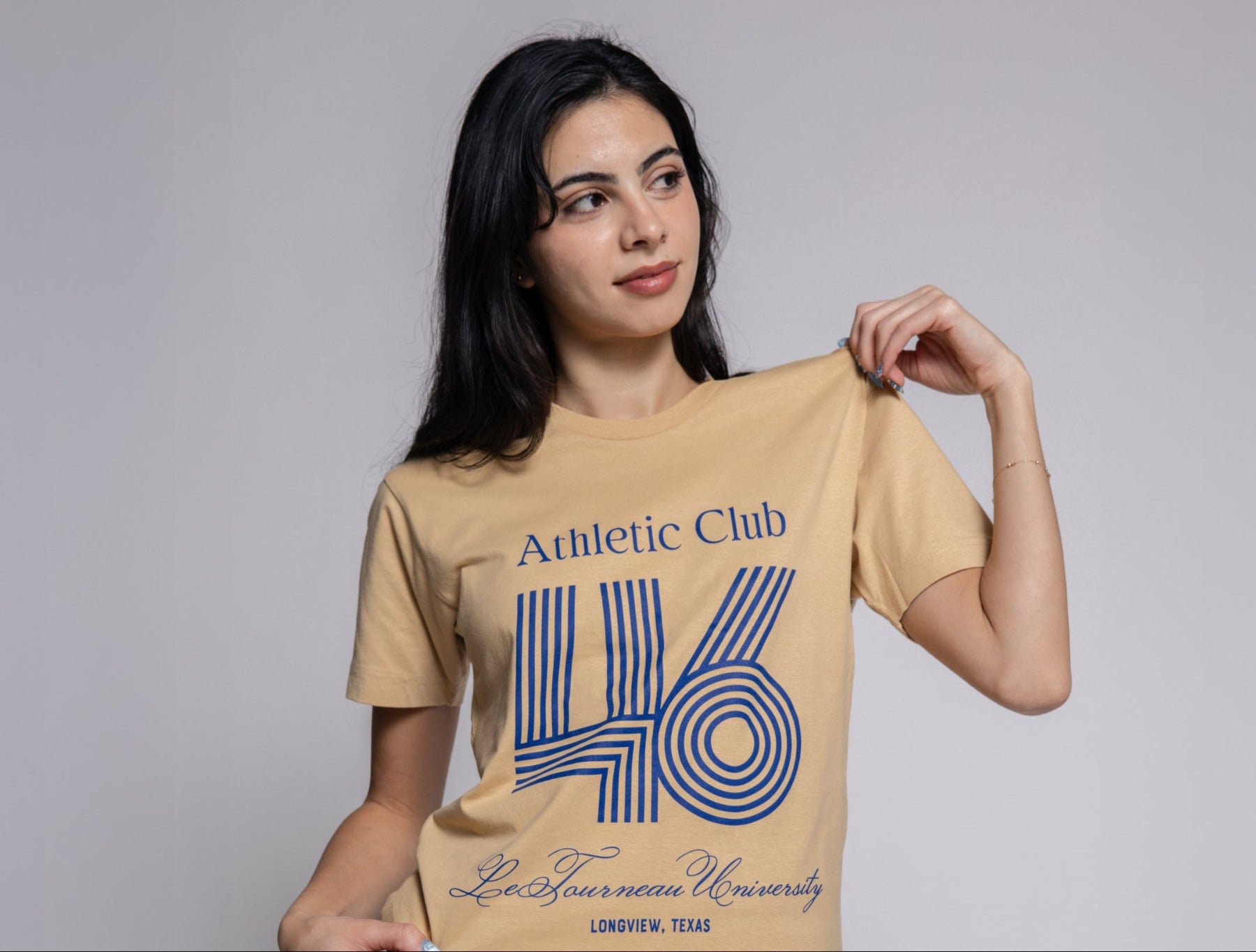 Woman wearing a beige t-shirt with blue text and numbers on a gray background